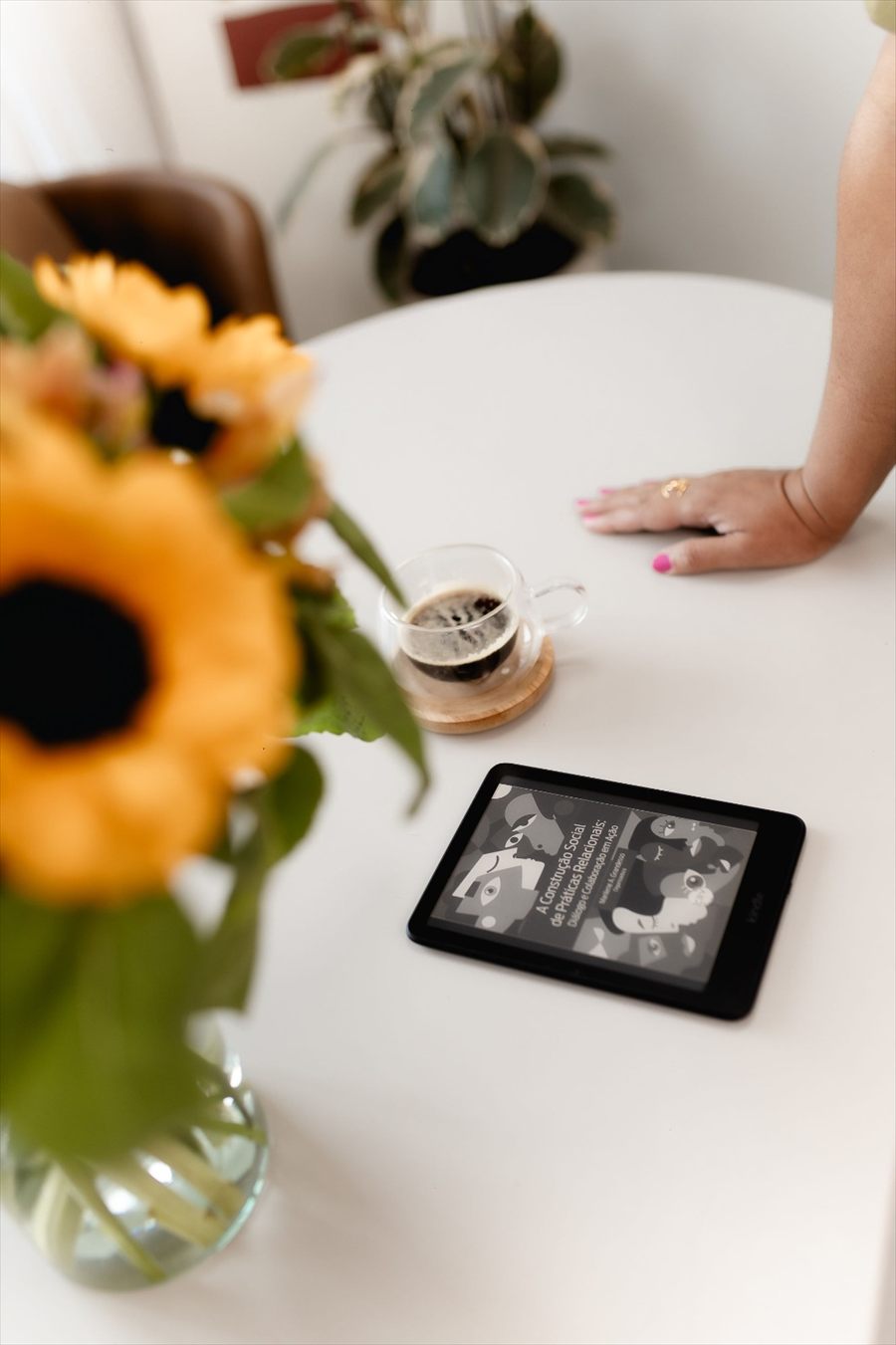 Mesa de atendimento de Nanci, com um café, flores e um livro sobre práticas relacionais